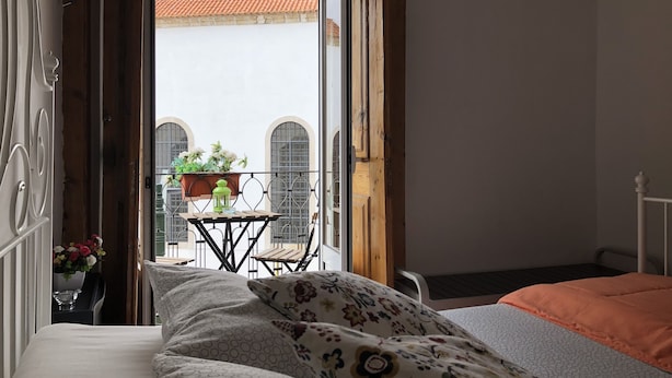 A bedroom with a bed, a window, and a view of a balcony with a table and potted plants. - Hostel Charme da Graça (Lisbon)