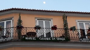 A building with a sign reading "HOSTEL CHARME DA GRAÇA" and a balcony with potted plants. - Hostel Charme da Graça (Lisbon)