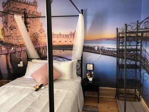 Un dormitorio con cama con dosel, una mesita de noche con un florero y un mural de un castillo y un puente.