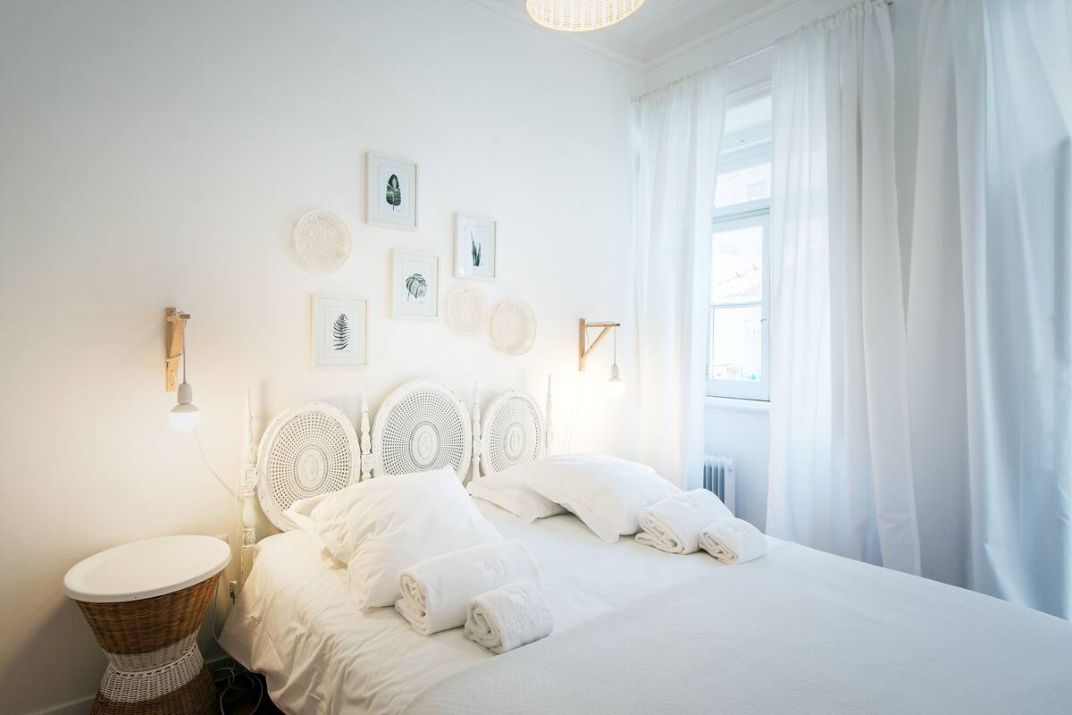 Un dormitorio blanco con cama, cortinas blancas y luces fijadas a la pared.
