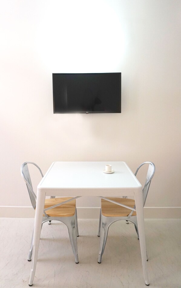 A white table with two chairs, a small cup on the table, and a flat-screen TV mounted on the wall. - Cozy Lisbon Janelas Verdes (Lisbon)