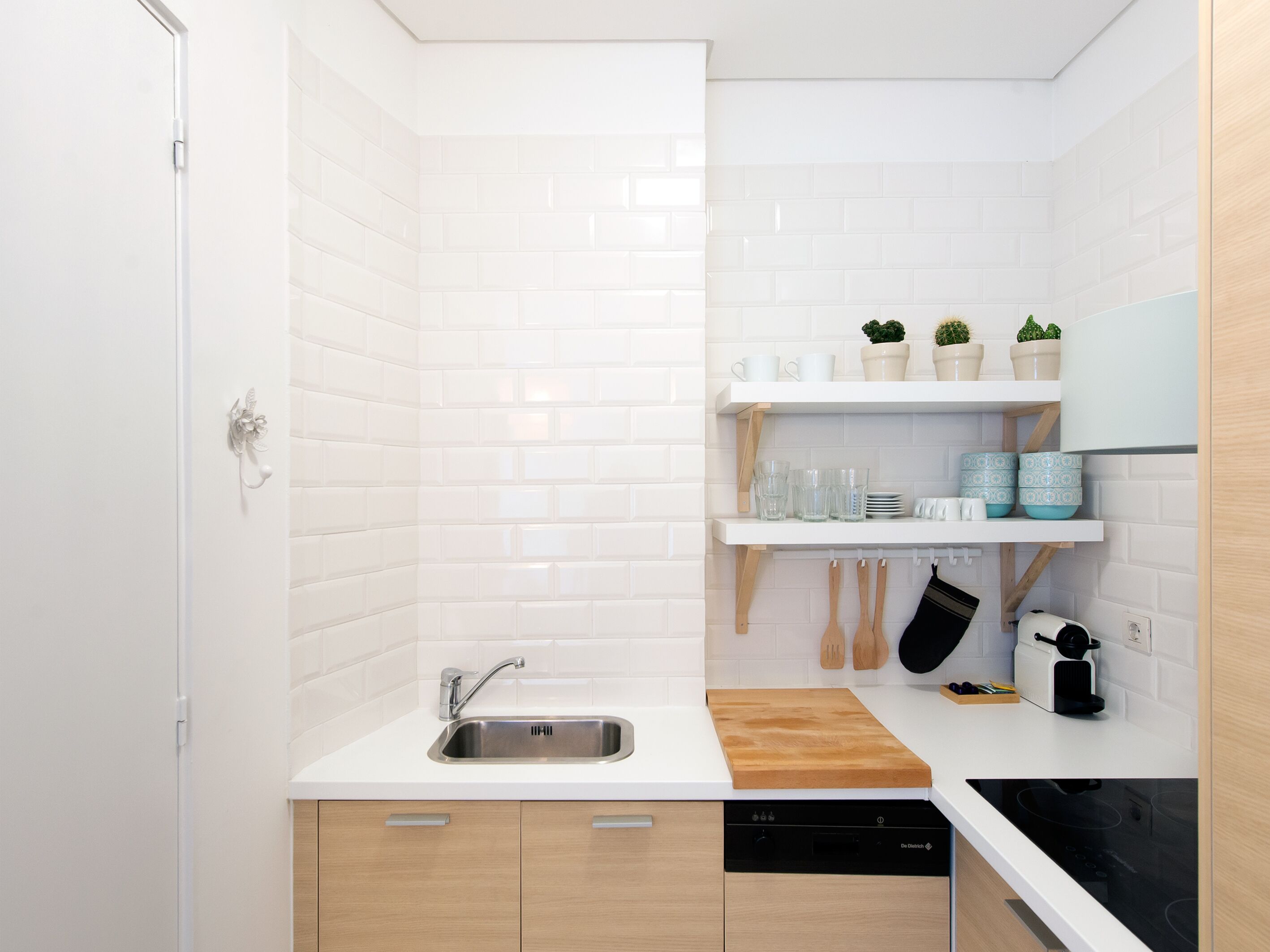 A compact kitchen with white subway tiles, a stainless steel sink, wooden cabinets, and a black dishwasher.
