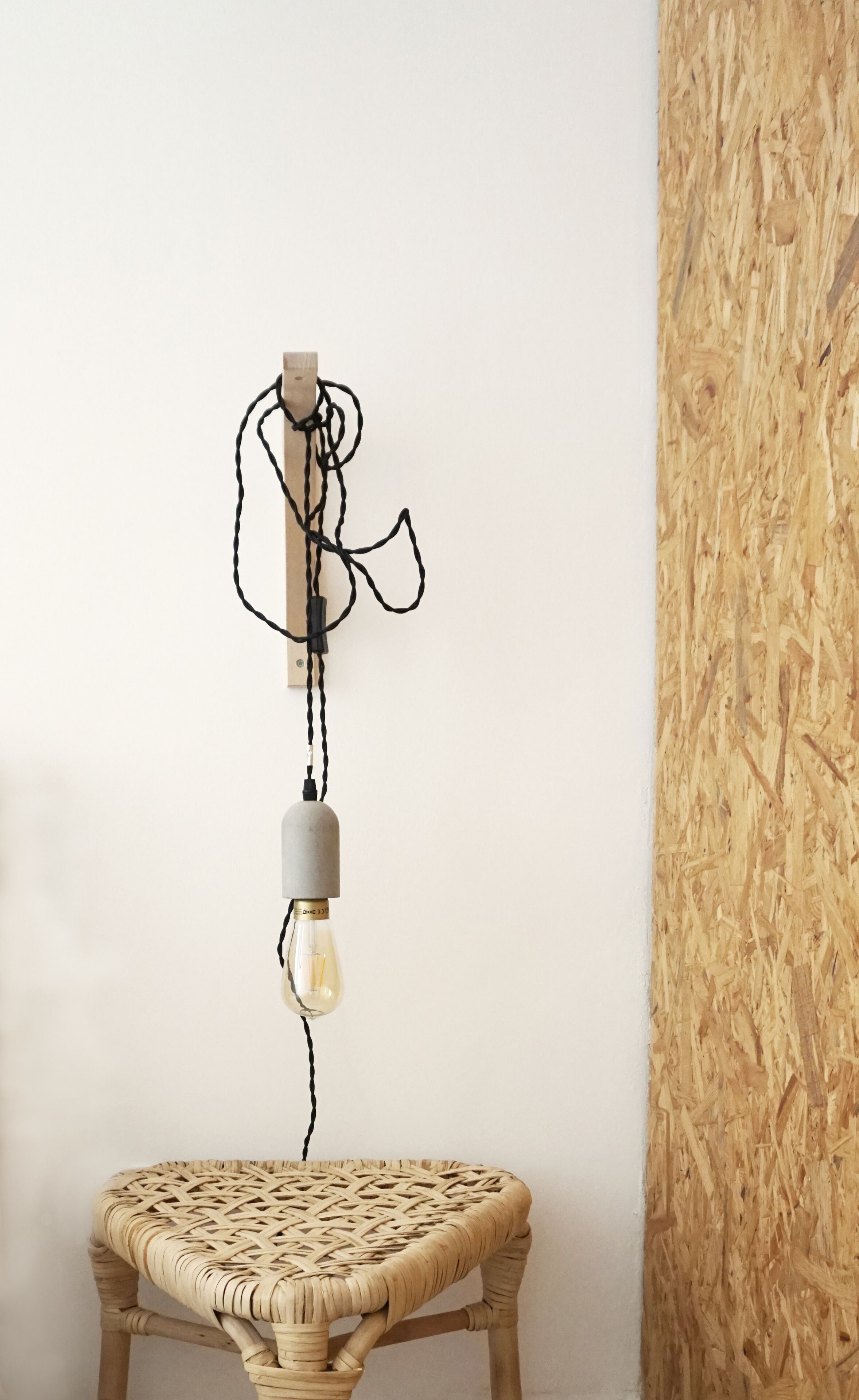 Un luminaire mural fixé au mur, doté d’une seule ampoule, une chaise en osier et un panneau mural en bois.