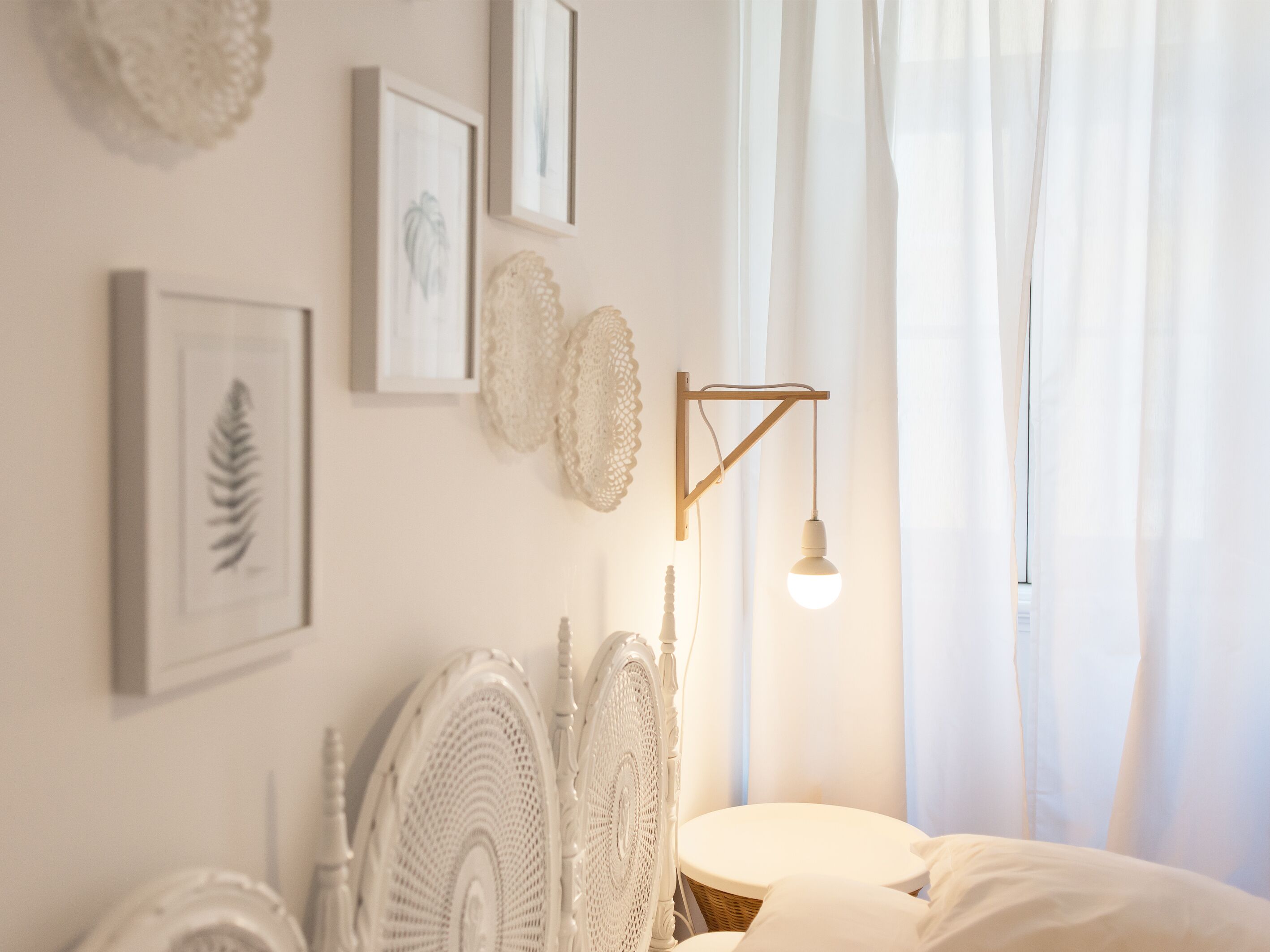 A bedroom with a white bed, a wall-mounted lamp, and framed artwork.
