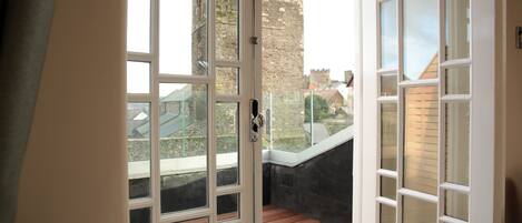 A room with a large window, a wooden floor, and a view of a castle.