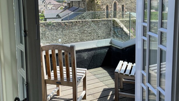 A balcony with a view of a stone tower and surrounding buildings. - Y Capel (Conwy)