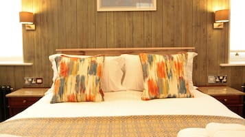Una cama bien hecha con ropa de cama estampada, paredes de paneles de madera y dos lámparas fijadas a la pared.