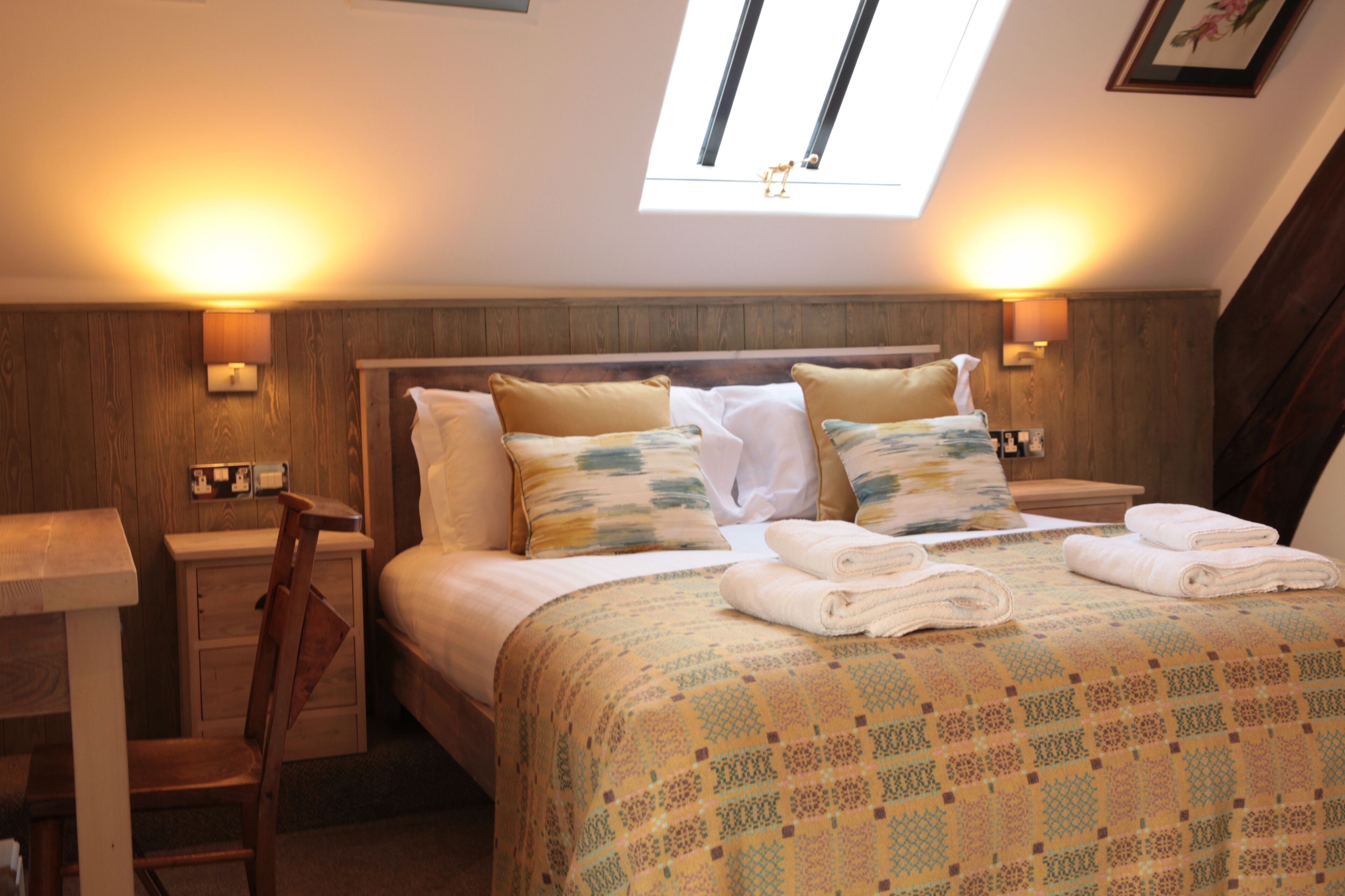 A bedroom with a wooden headboard, a bed with patterned bedding, two bedside lamps, and a skylight.