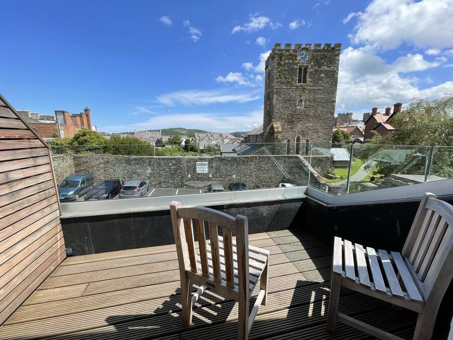 A wooden deck with two chairs, a stone wall, and a tower in the background.