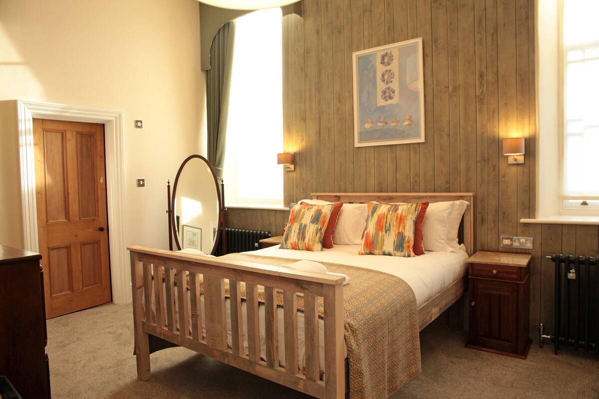 Une chambre à coucher avec un lit en bois, une table de chevet, une commode, un miroir et un tableau encadré accroché au mur.