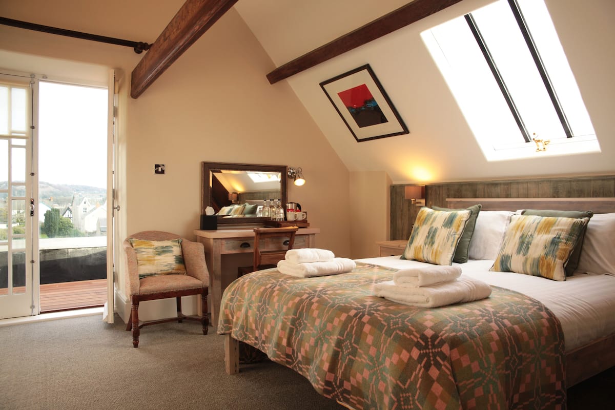 Une chambre à coucher comprenant un lit, un bureau, une chaise, un grand miroir et un balcon avec vue.