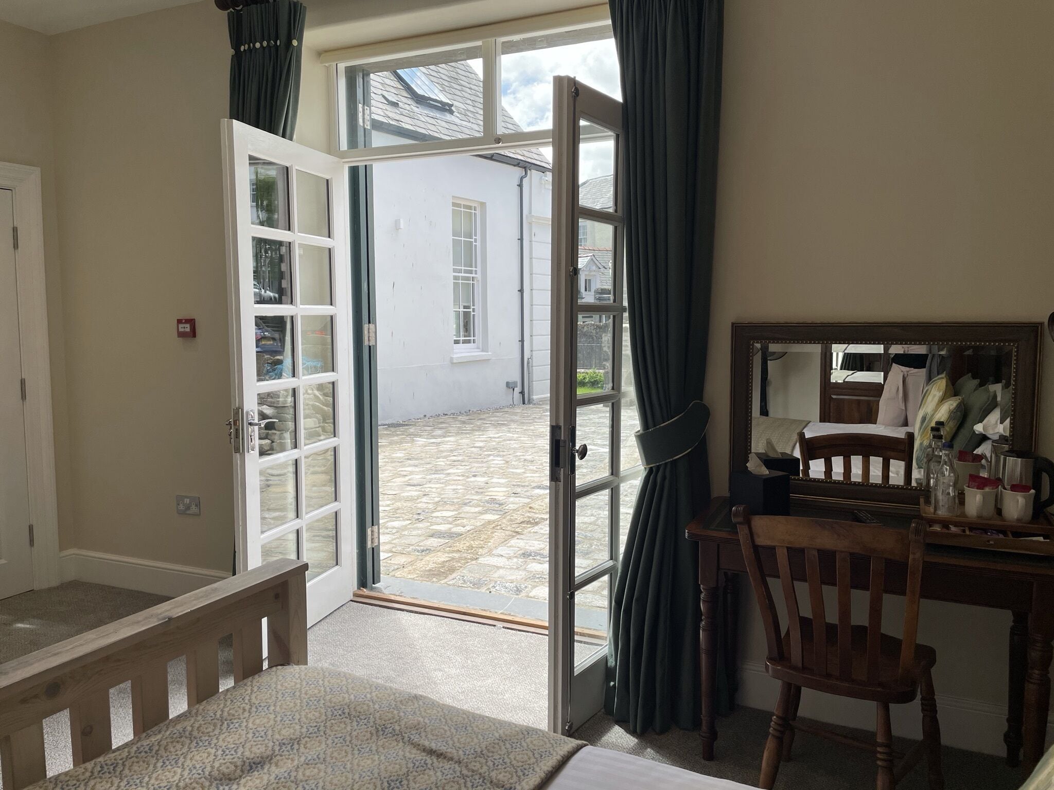 A room with a bed, a desk, a chair, and an open door leading to a courtyard.