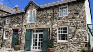 A stone building with a central entrance, two windows on the upper floor, and a chimney. - Y Capel (Conwy)