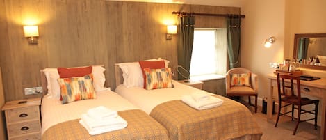 A hotel room with two beds, a desk, a chair, and a mirror.