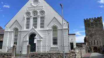 A white building with a triangular roof, a clock tower, and a stone wall.