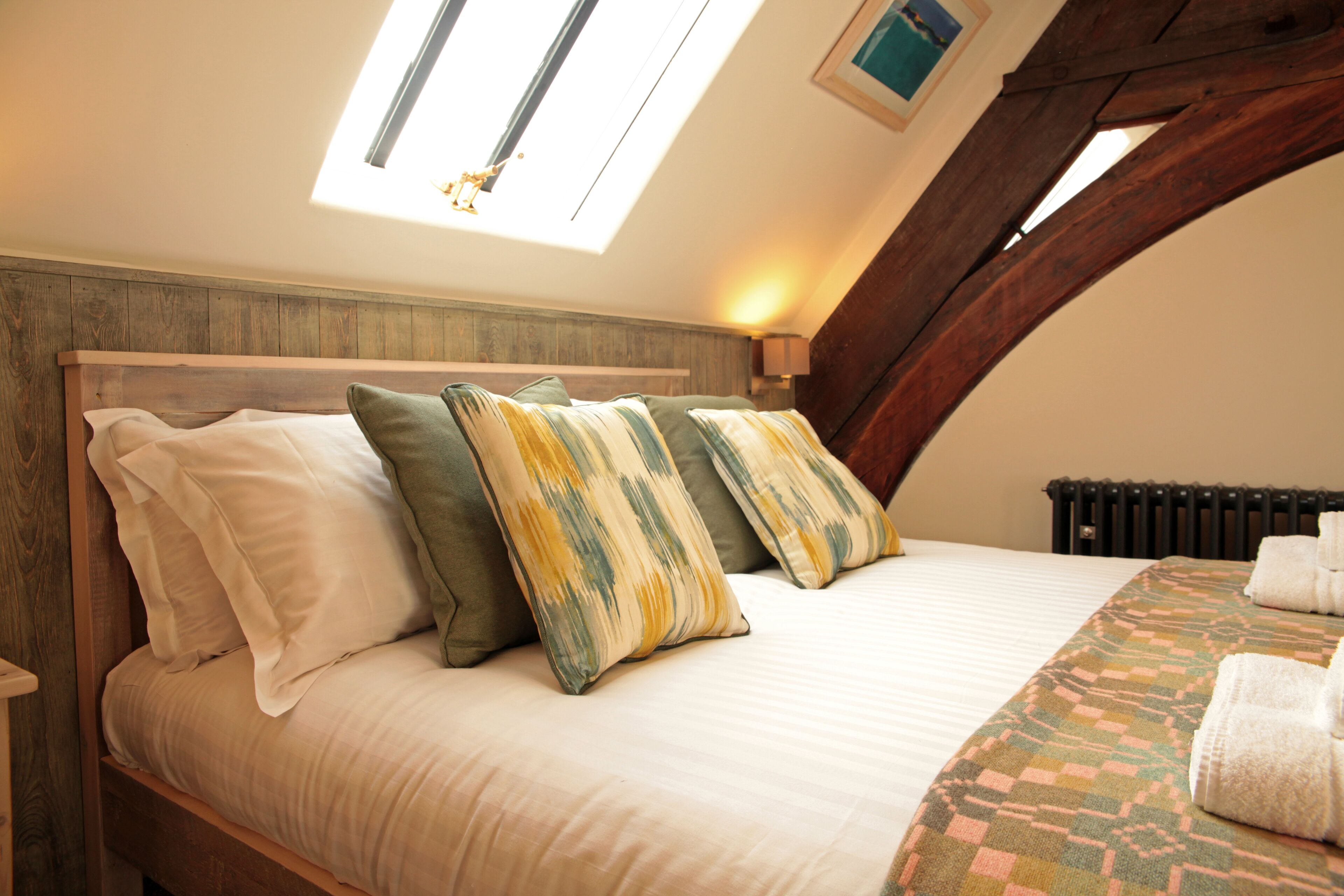 A bedroom with a wooden headboard, a skylight, and a patterned bedspread.