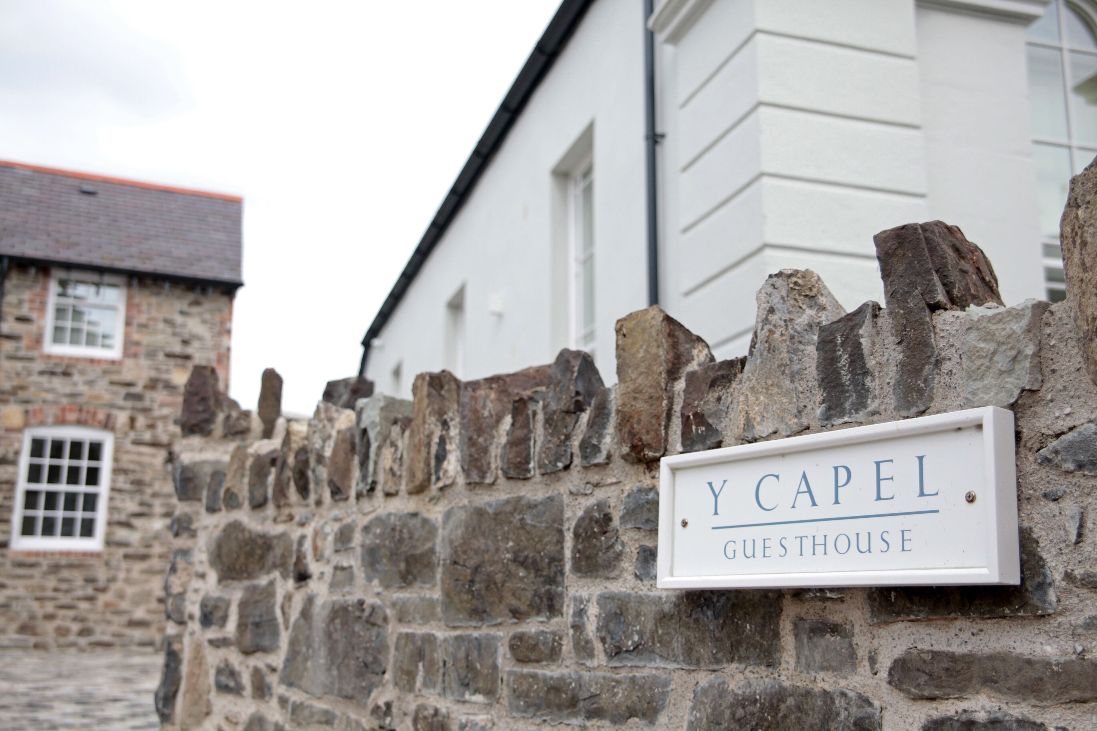 Een stenen muur met een bord waarop staat 'Y CAPEL GUESTHOUSE'.