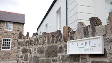 Een stenen muur met een bord waarop staat 'Y CAPEL GUESTHOUSE'.