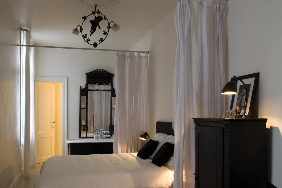 A bedroom with a large bed, a bedside table, a dresser, a mirror, and a ceiling light fixture.
