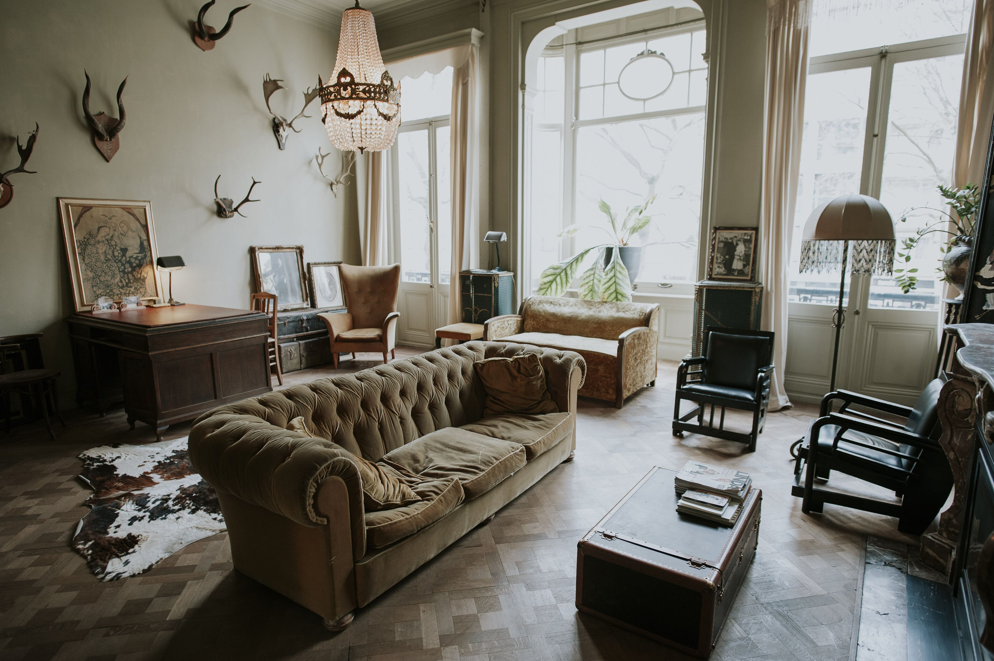 A spacious living room with a large brown sofa, a wooden coffee table, and a chandelier. There are several chairs and a potted plant.