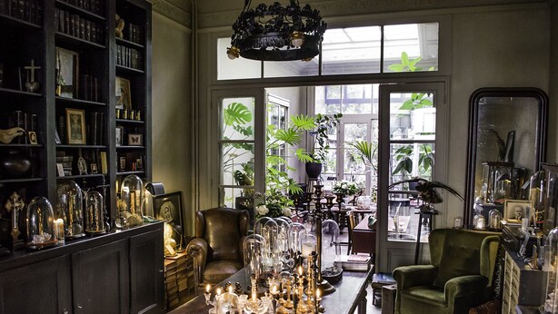 A room with a large bookshelf, a dining table with candles, and a green armchair. - Boulevard Leopold Rooms & Suites (Antwerp)