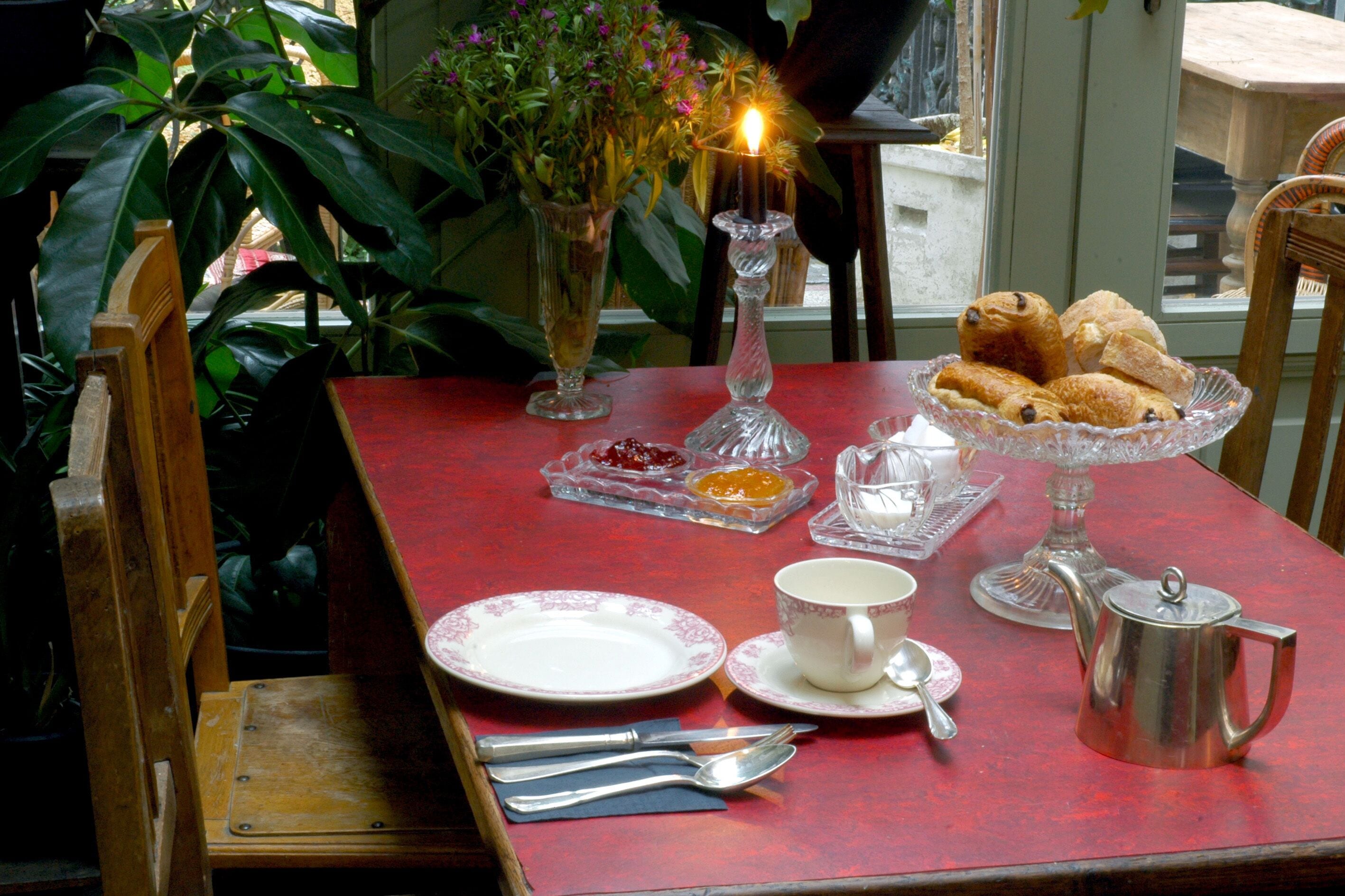 Een ontbijttafel met gebak, een theepot en een bloevas.