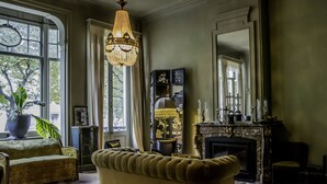 A room with a large window, a chandelier, a fireplace, and a sofa. - Boulevard Leopold Rooms & Suites (Antwerp)