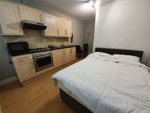 A compact hotel room with a kitchenette, a bed, and a bedside table.