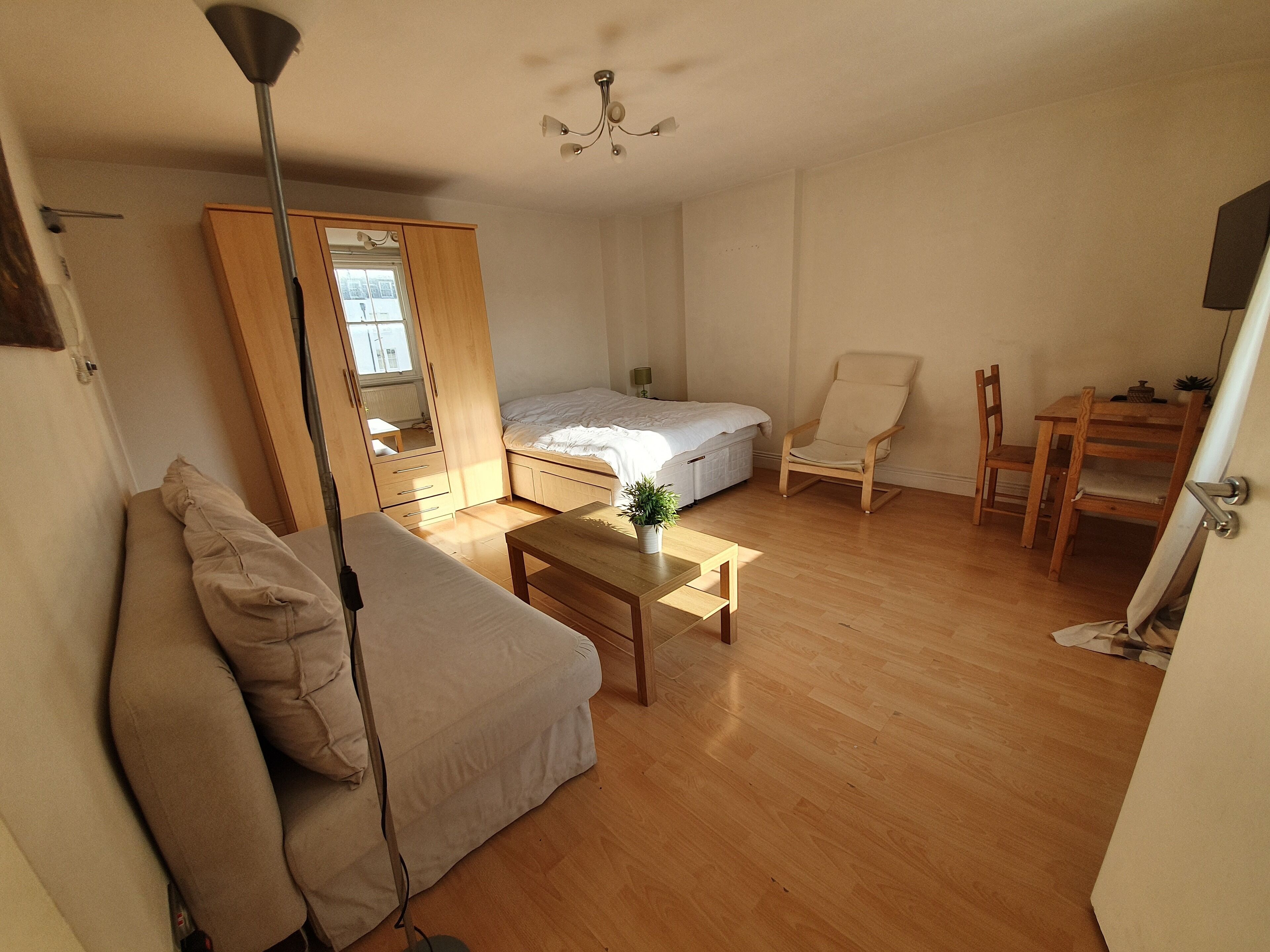 A compact room with a bed, a sofa, a small table, a chair, and a desk.