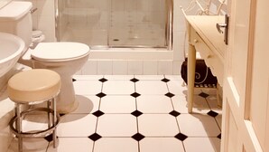 Un baño con ducha envuelta en vidrio, inodoro, lavabo y un taburete.
