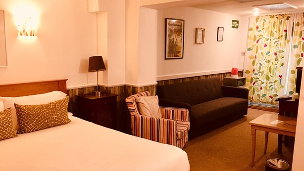 Una habitación de hotel con una cama grande, un sofá, un sillón a rayas, una mesita y un cubo de basura.