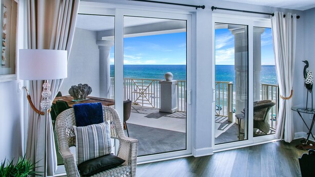 Una habitación con vista al océano, un balcón con mobiliario exterior y un amplio ventanal corredizo.