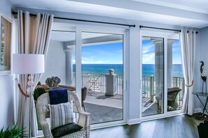 Una habitación con vista al océano, un balcón con mobiliario exterior y un amplio ventanal corredizo.