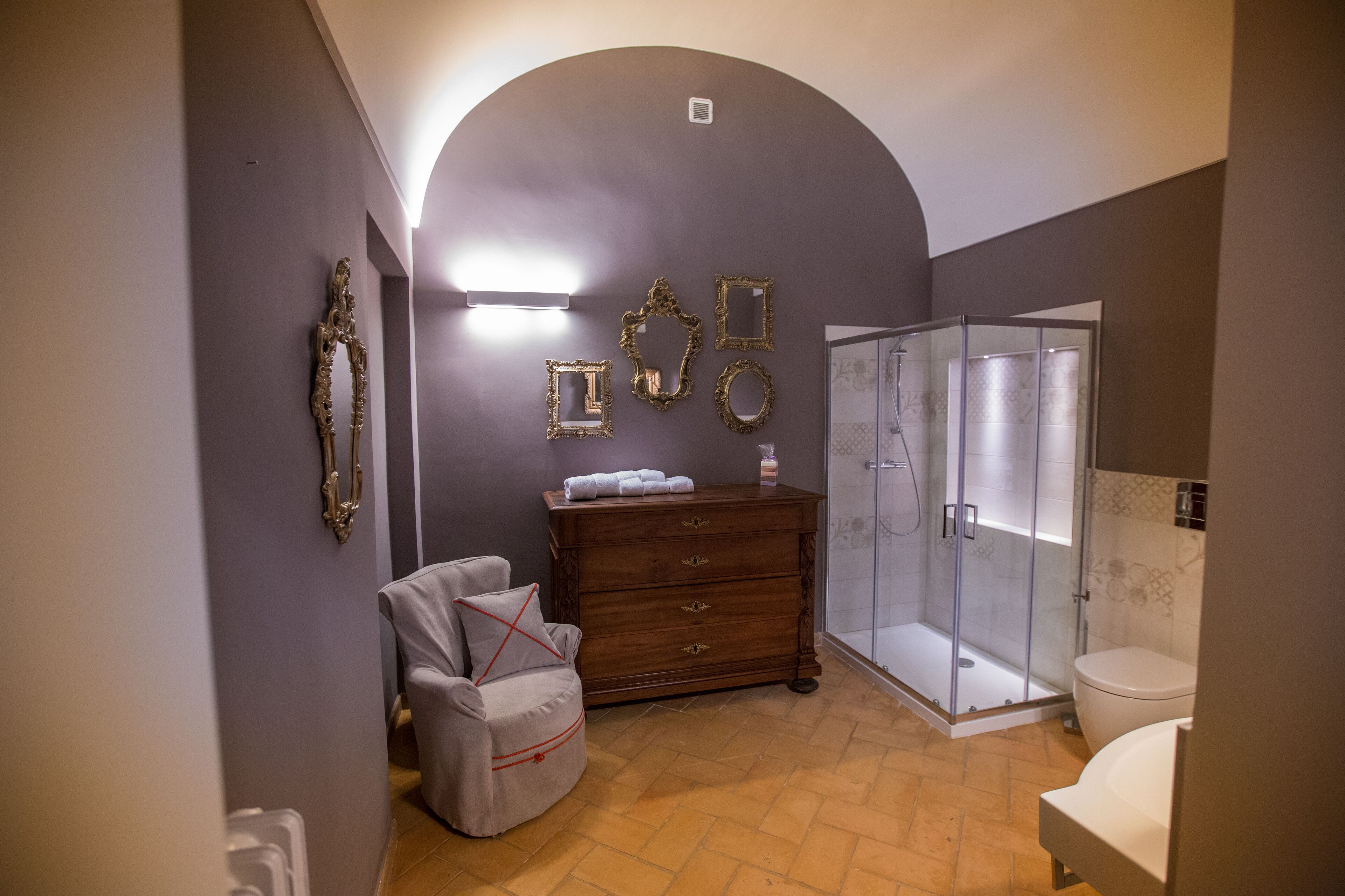 Ein Badezimmer mit Dusche, Toilette, Waschtisch und einem Sessel.