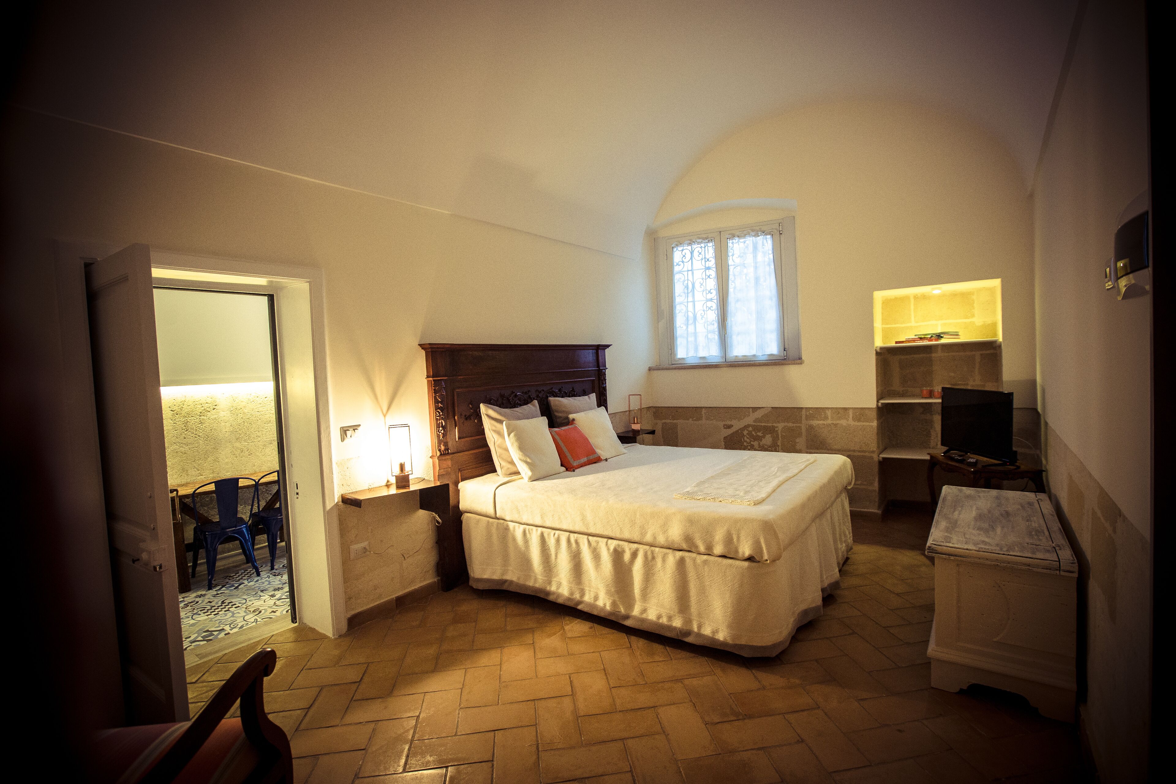 A bedroom with a bed, a nightstand, a TV, and a window.