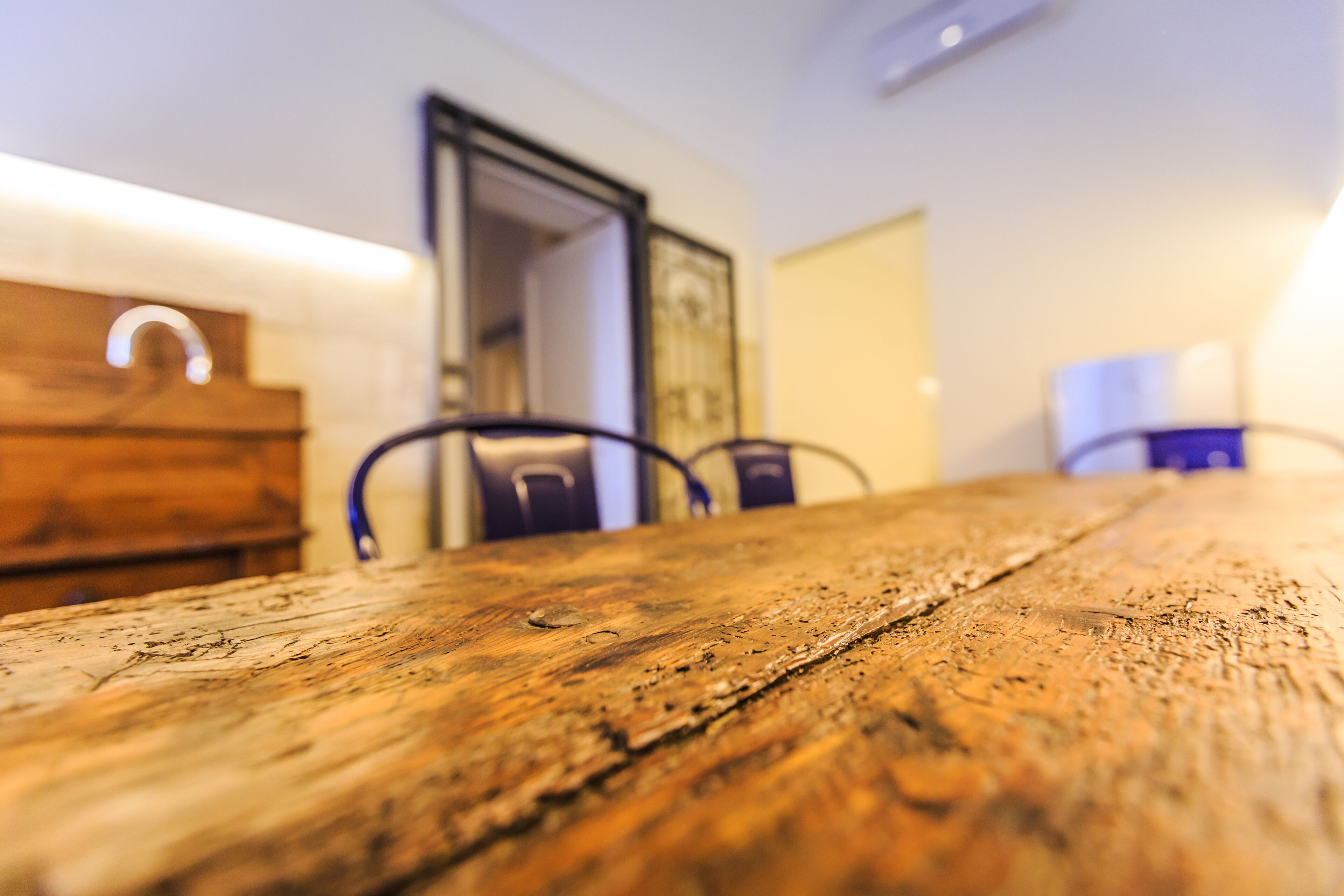 A wooden table with visible wear and tear, surrounded by chairs.