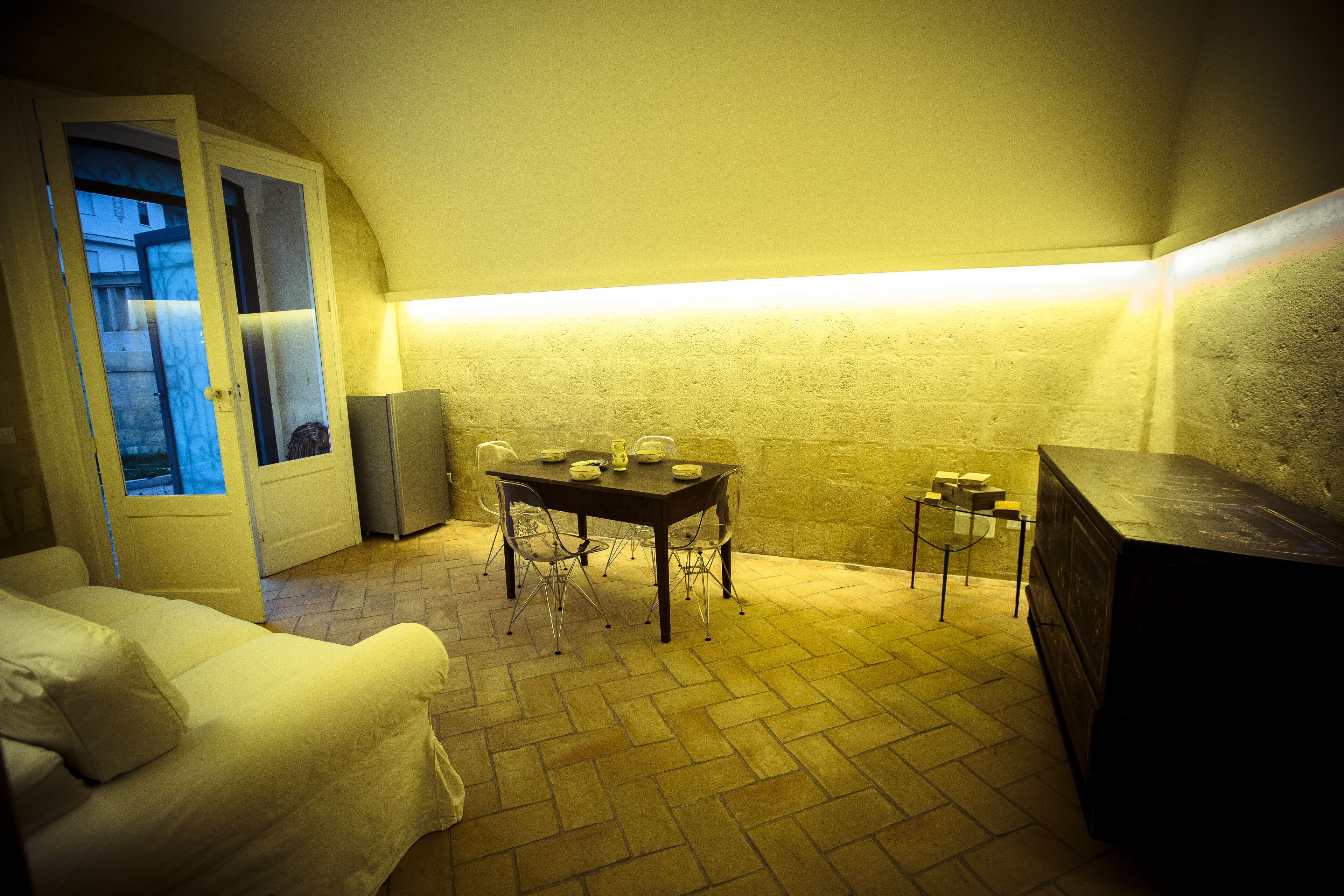 A cozy room with a bed, a table with chairs, a small cabinet, and a door leading to an outdoor area.