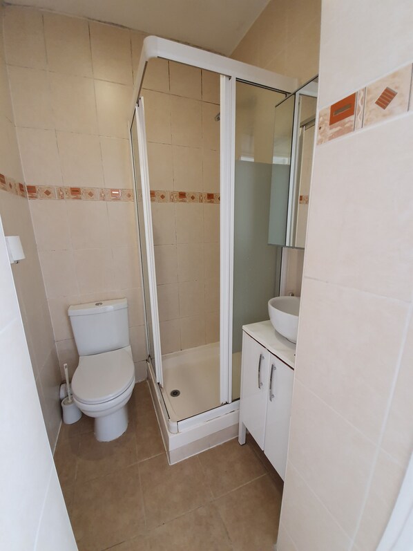 A bathroom with a toilet, a glass-enclosed shower, and a sink with a mirror. - Studio Apartment in South Kensington 3 (London)