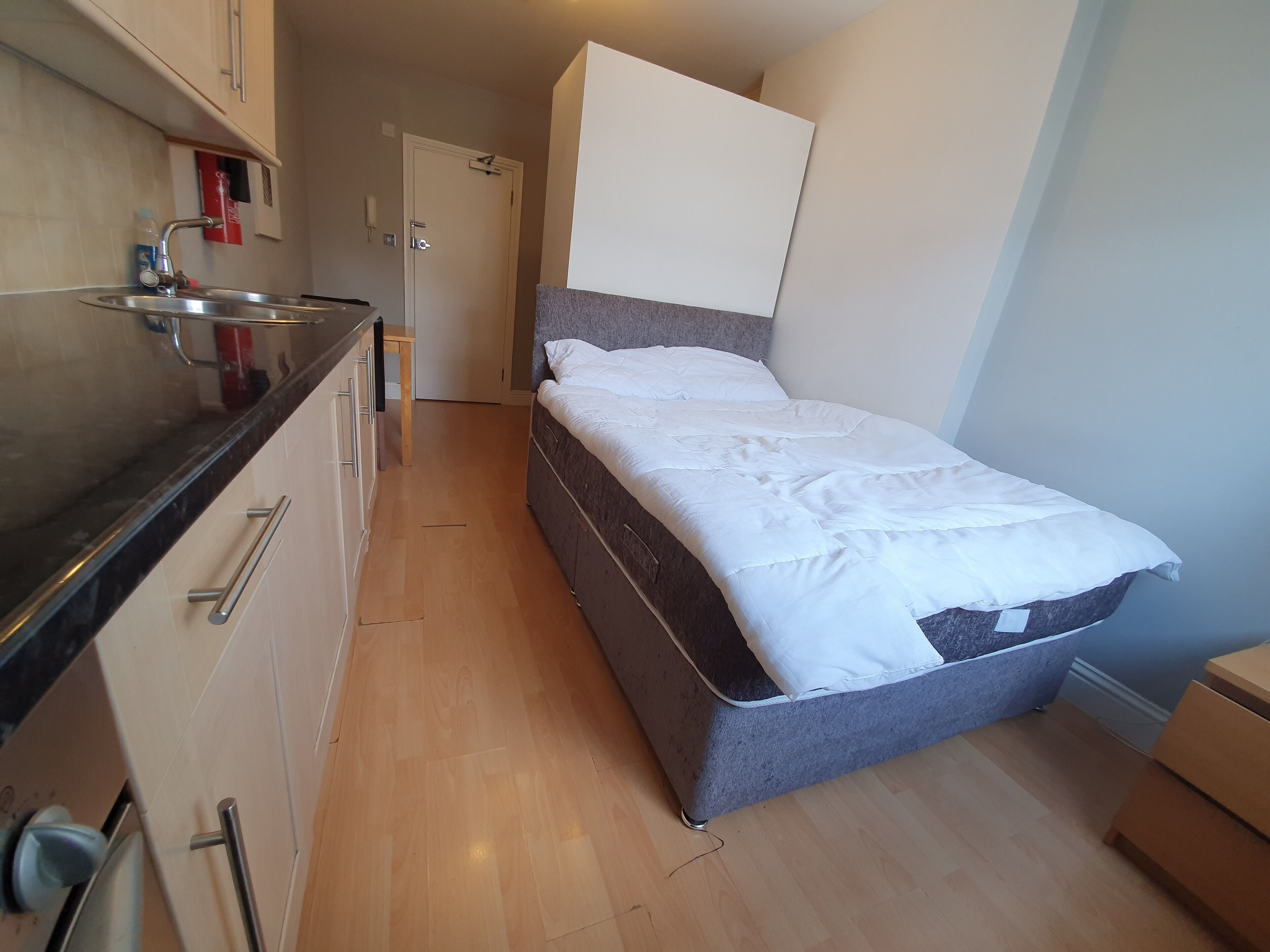 A compact room with a kitchenette, a bed, and a door leading to another room.