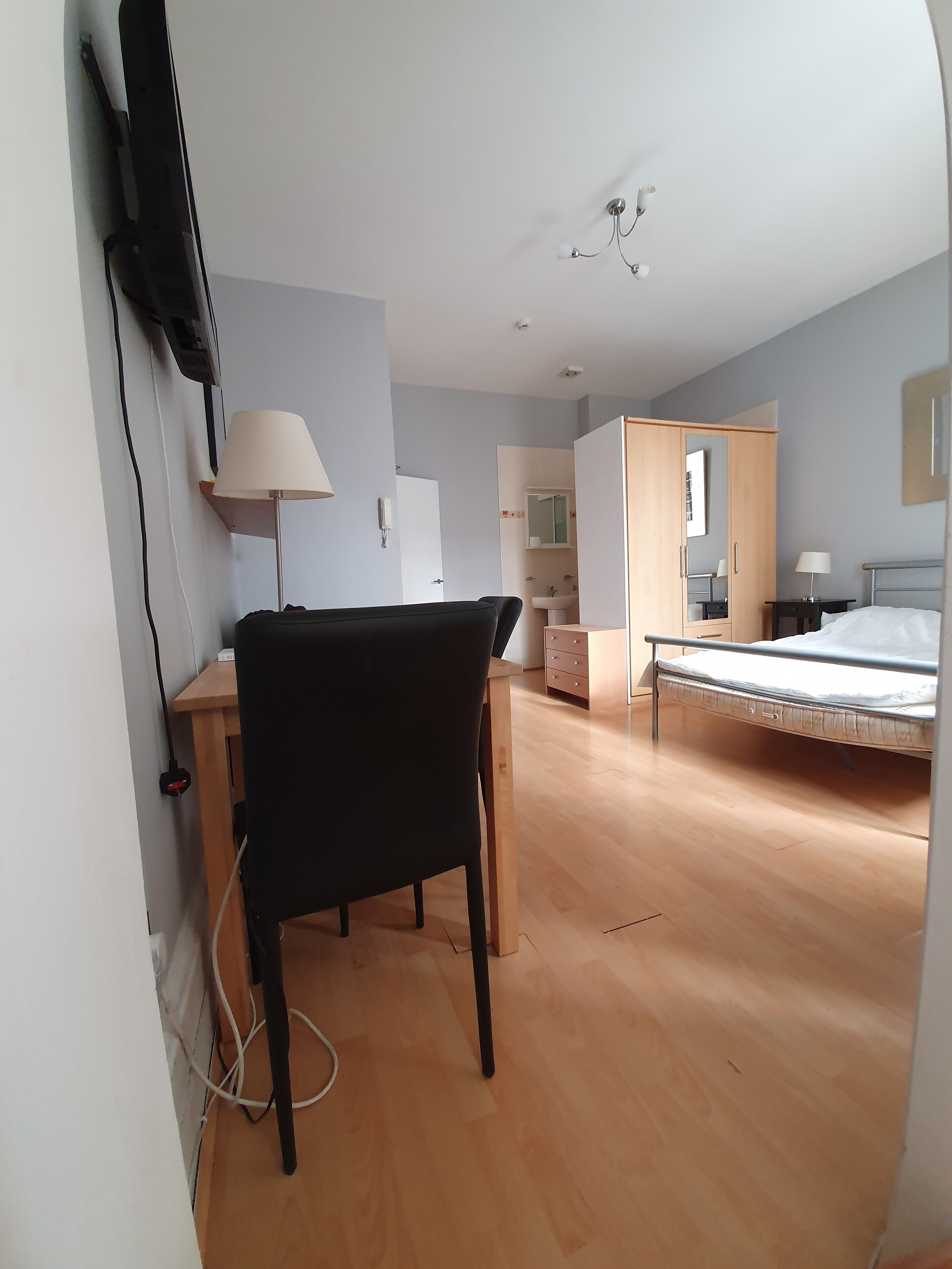 A hotel room with a bed, a desk, a chair, a lamp, and a wardrobe.