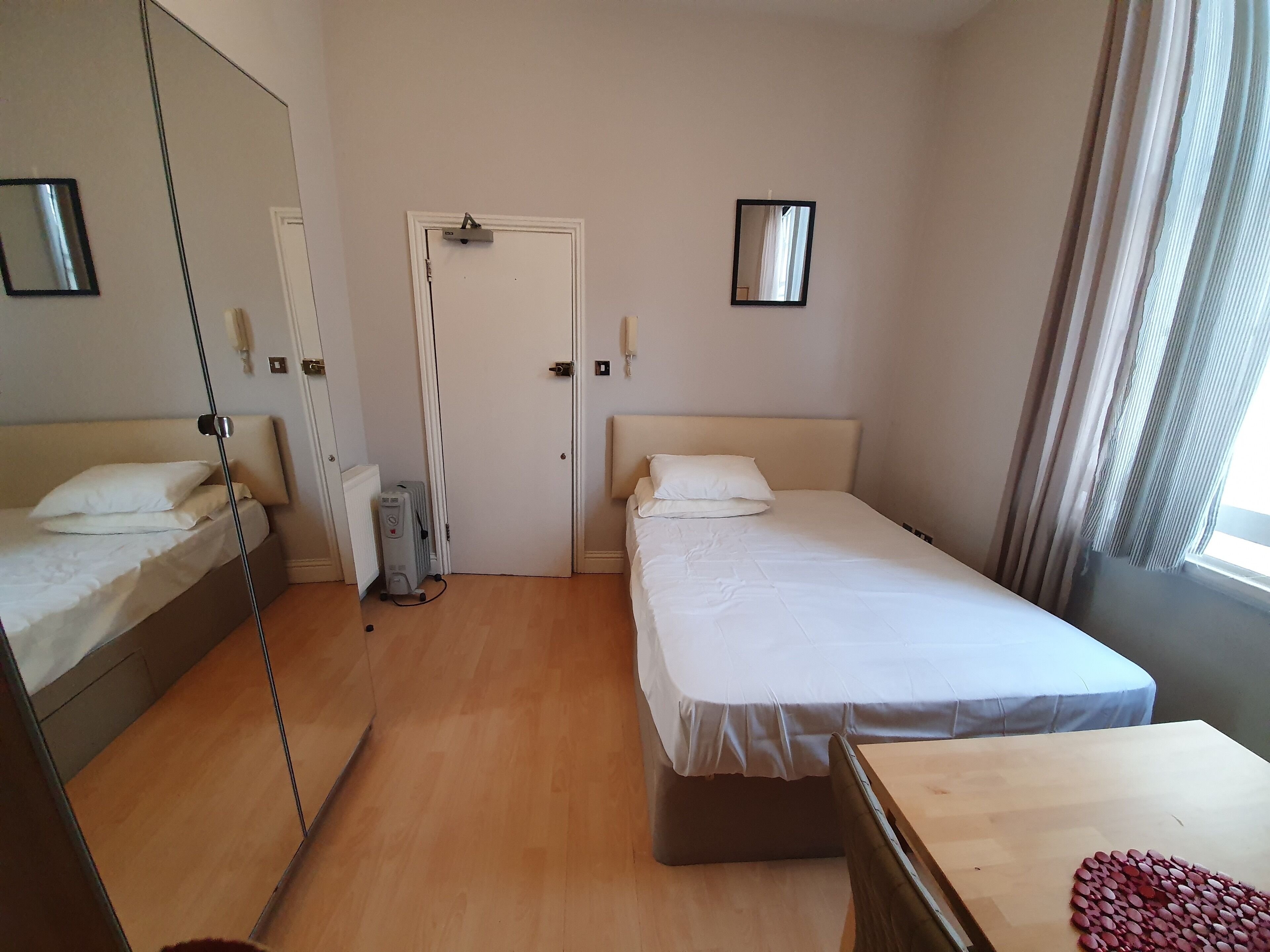 A hotel room with two single beds, a wooden table, a radiator, and a mirror on the wall.