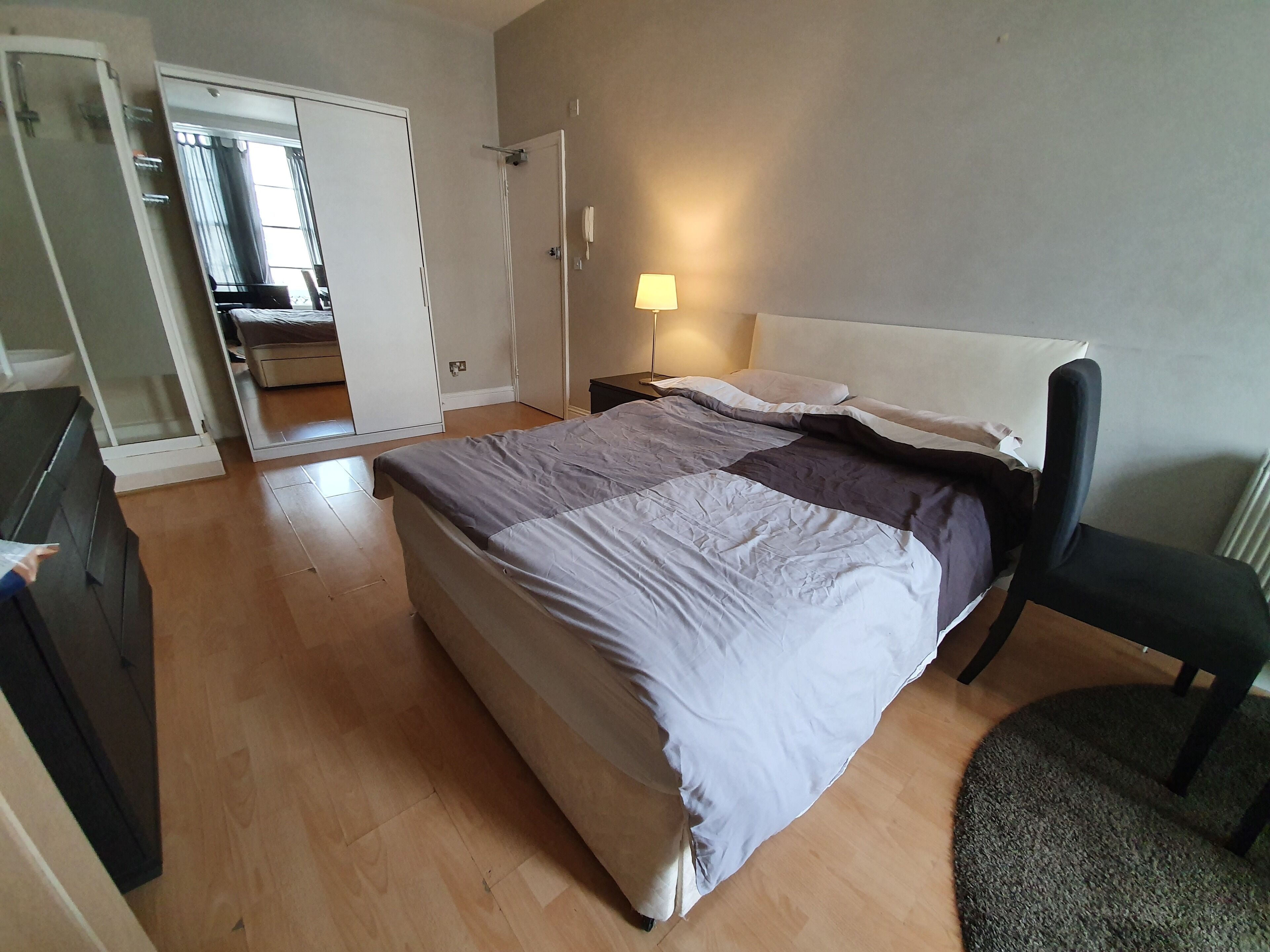 Et soveværelse med seng, stol, natbord, lampe og garderobeskab.