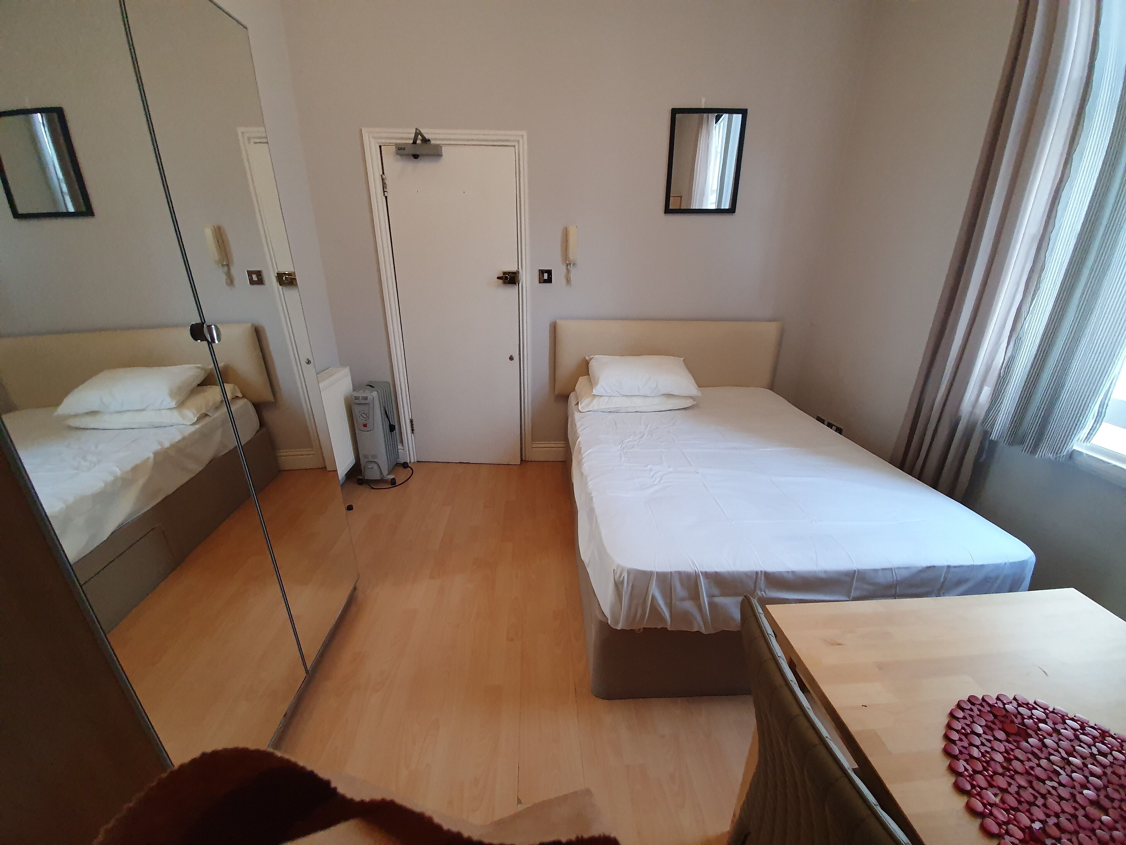Une chambre d’hôtel avec deux lits, un radiateur, un miroir et une fenêtre avec des rideaux.