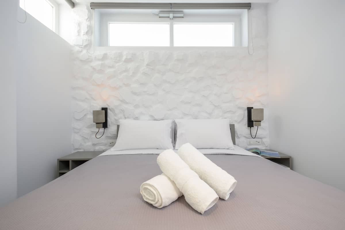Una cama bien hecha con sábanas y toallas blancas, un cabecero con estampado de piedra y lámparas de noche.