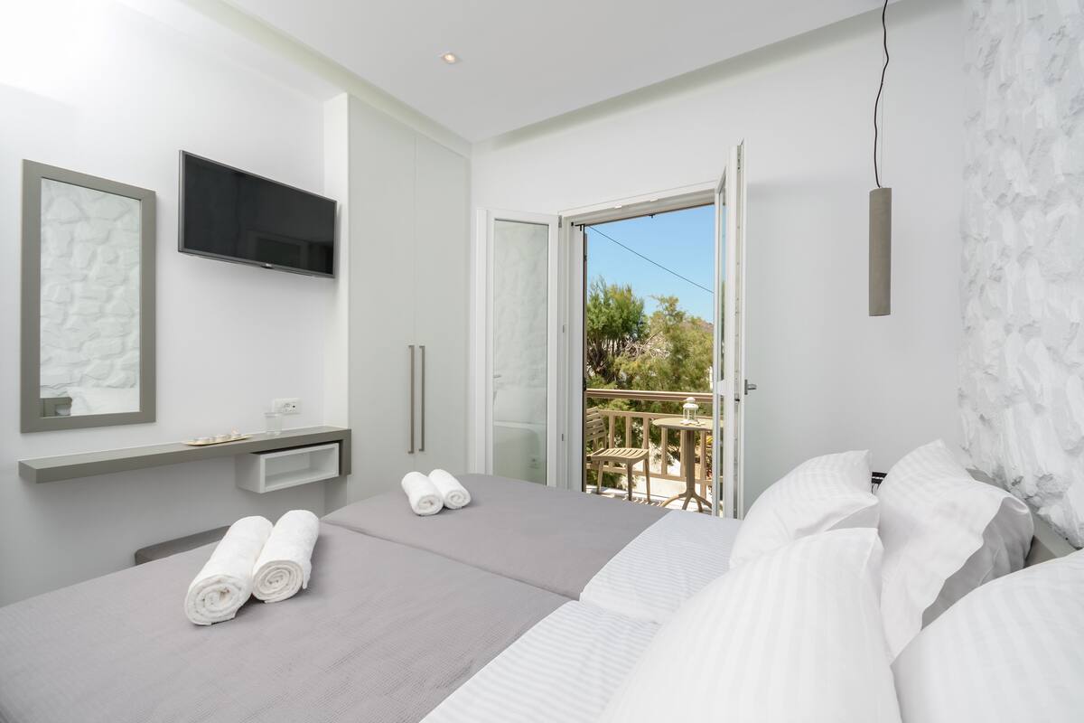 Una habitación de hotel moderna con una cama grande, un televisor en la pared y un balcón con mesa y sillas.