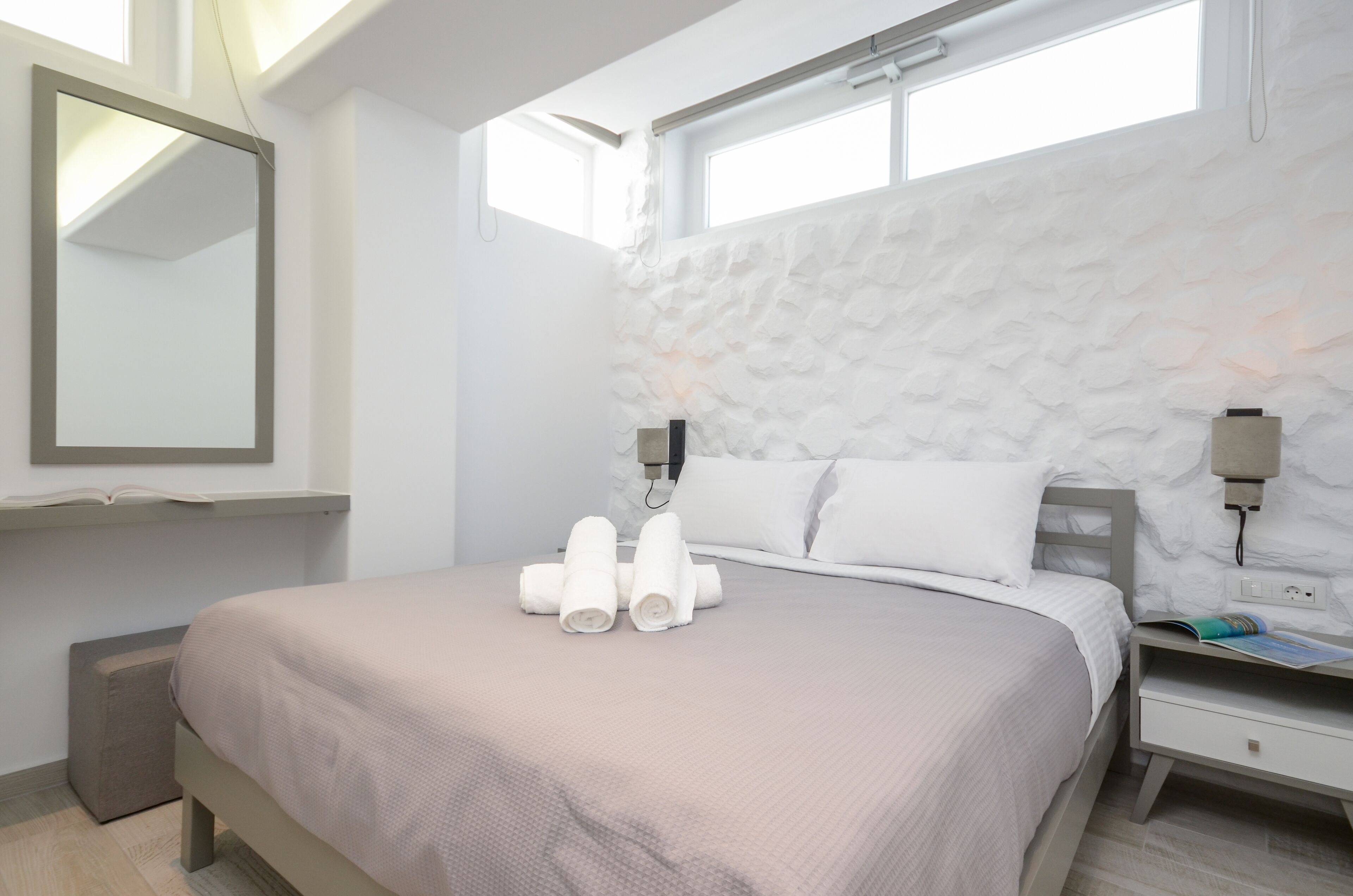 Ein modernes Hotelzimmer mit einem großen Bett, einem wandmontierten Spiegel und einem Fenster mit Tageslicht.