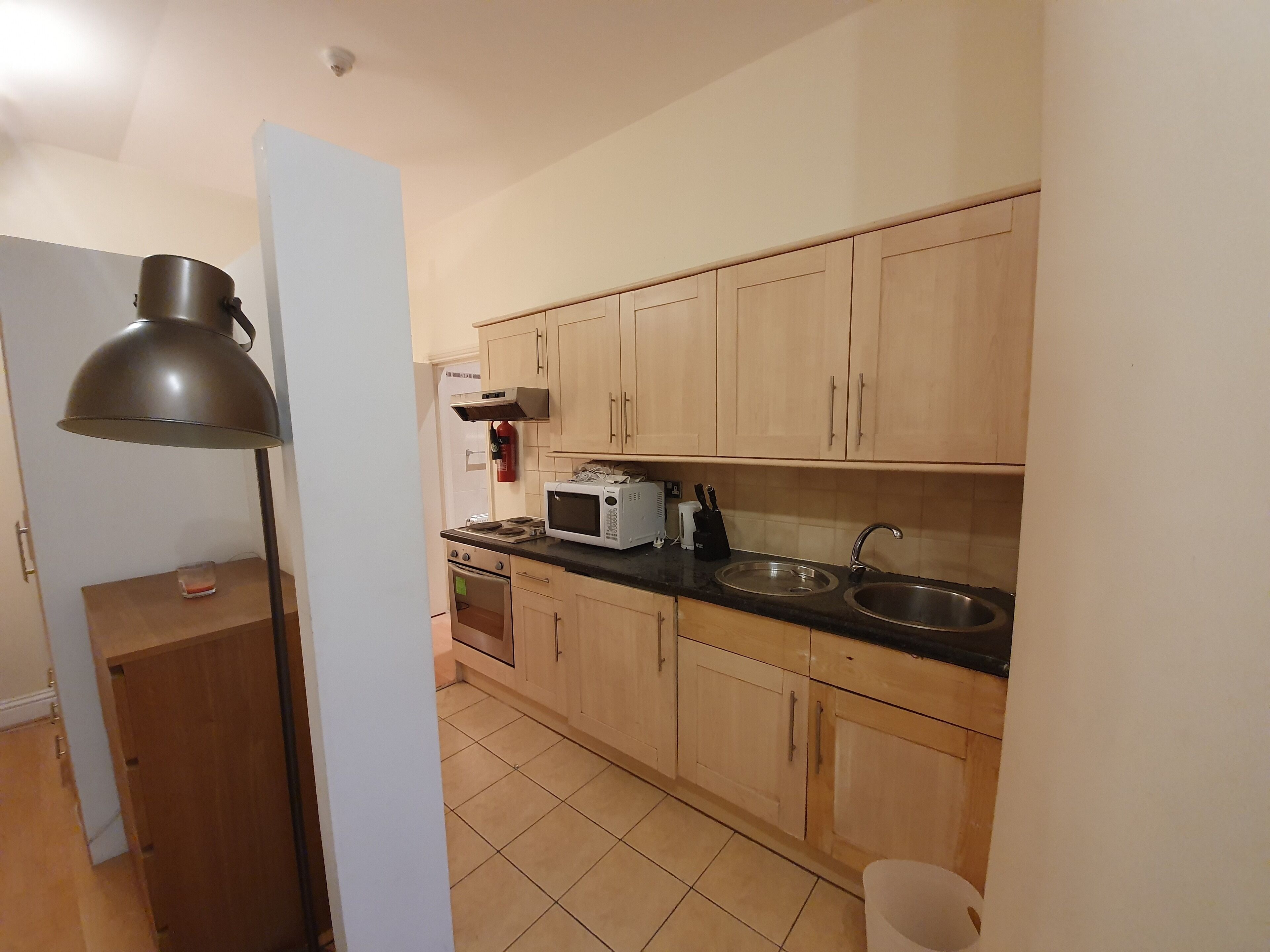 A kitchen with wooden cabinets, a microwave, a stove, a sink, and a floor lamp.