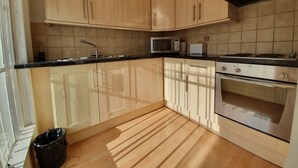 Une cuisine avec des armoires en bois, un four à micro-ondes, une cuisinière et une poubelle.