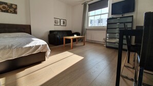Une chambre d’hôtel avec un lit, une table en bois, un canapé en cuir noir, une télévision et une fenêtre avec des rideaux.
