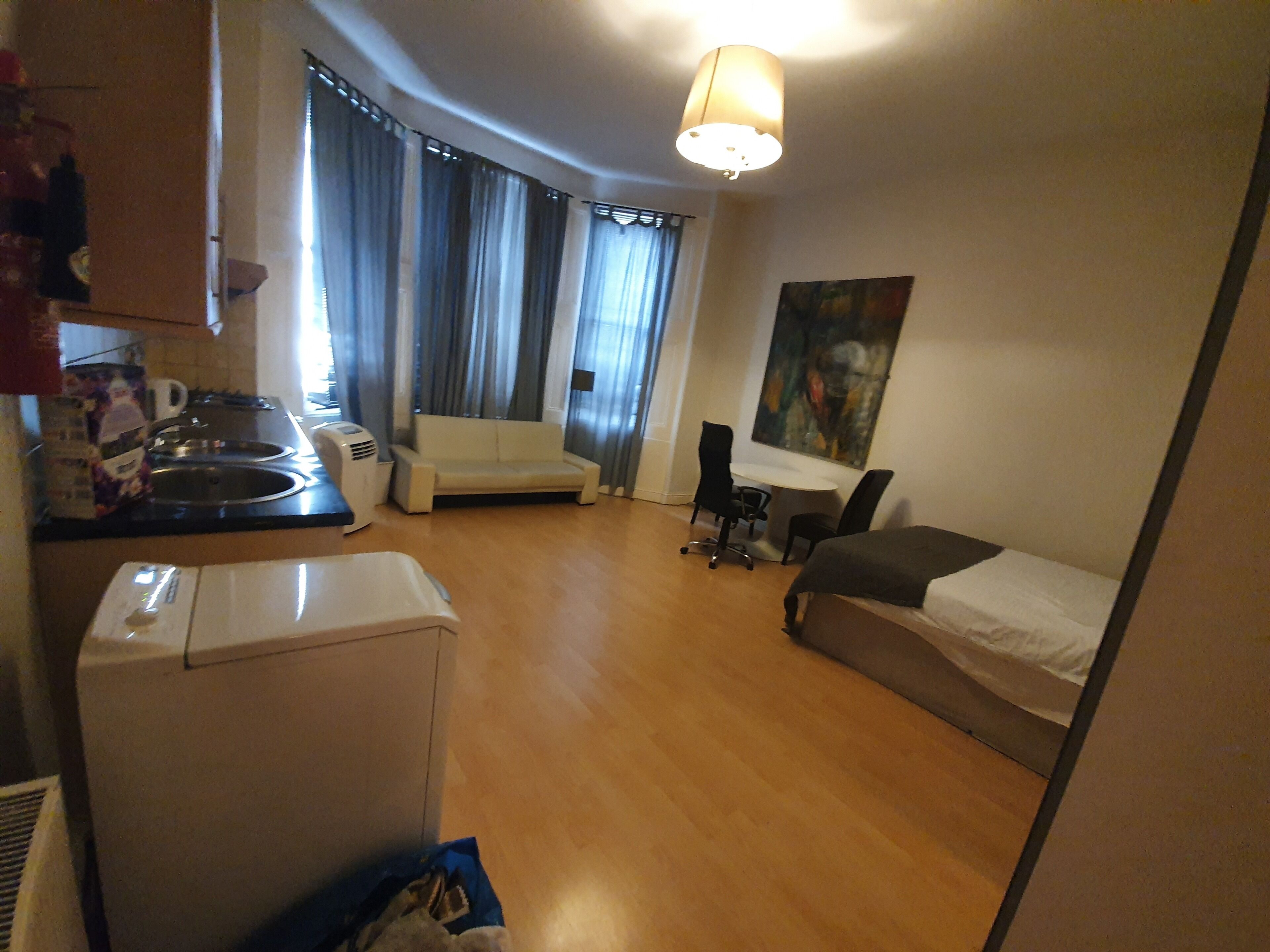 A compact hotel room with a kitchenette, a sofa, a bed, and a desk.